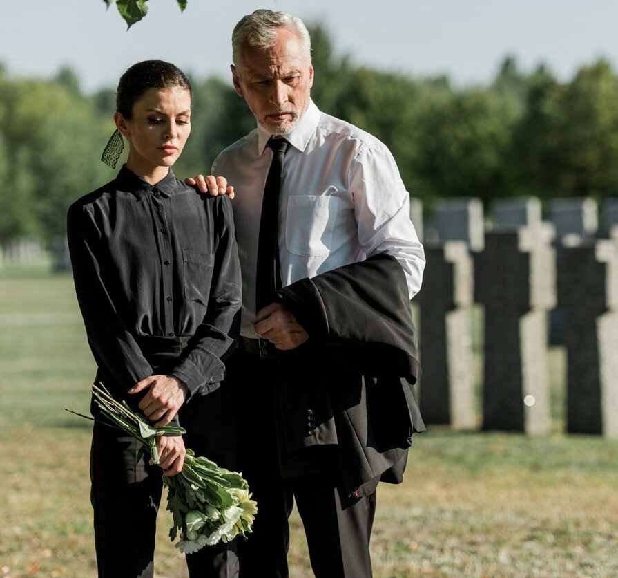 senior man standing with woman holding flowers on funeral