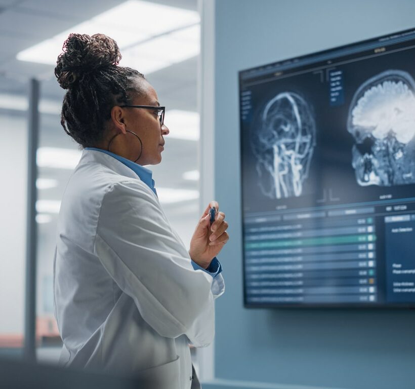 Female Neurologist looks at TV Screen with MRI Scan with Brain Images