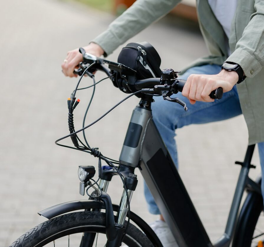 A person in casual attire is riding an electric bike along a well-maintained brick pathway in a park. The scene captures a sunny day, promoting outdoor activities and healthy living.